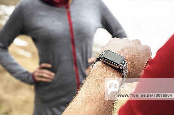 Male athlete checking time while woman standing in background during winter