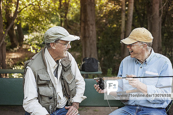 Fröhlicher älterer Mann unterhält sich mit einem Freund  während er Angelruten im Wald hält