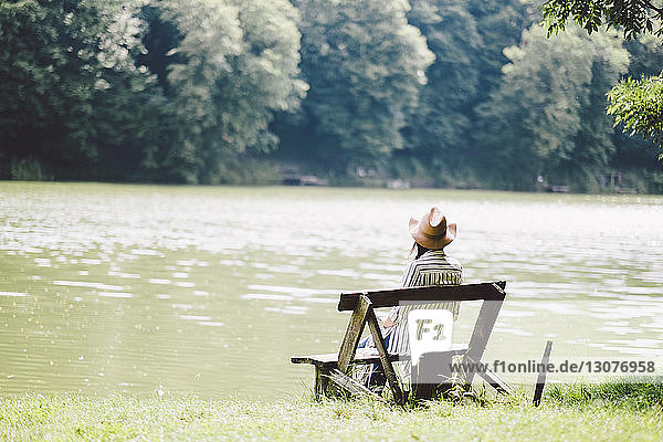 Rückansicht einer Frau  die auf einer Bank am Seeufer im Wald sitzt
