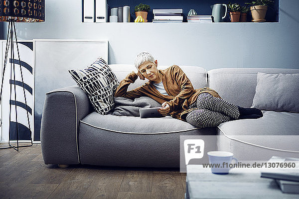 Frau benutzt Tabletten  während sie sich zu Hause auf dem Sofa entspannt