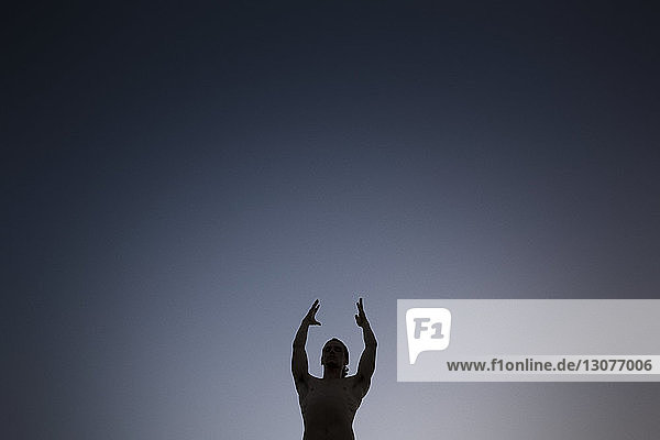 Niedrigwinkelansicht eines Mannes ohne Hemd  der mit erhobenen Armen steht  während er nachts gegen den Himmel meditiert