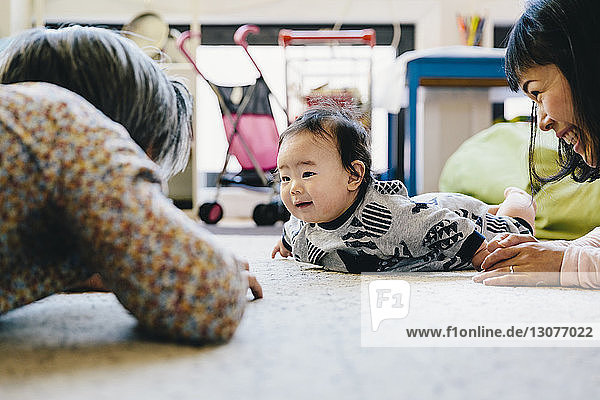 Happy mother and grandfather playing with cute baby boy lying on rug at home