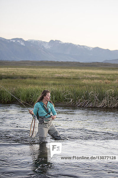 Young woman fly-fishing while standing in Owens River against mountains