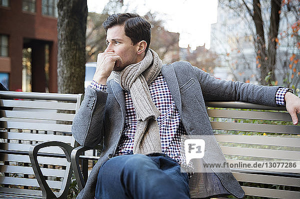 Nachdenklicher Mann schaut weg  während er sich auf einer Parkbank entspannt