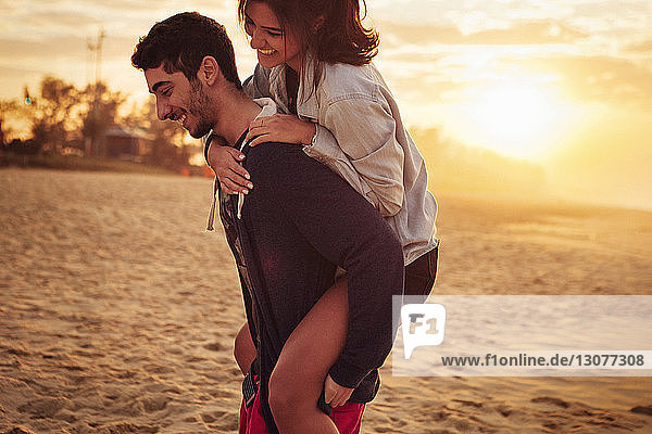 Mann nimmt seine Freundin am Strand Huckepack