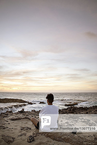 Rückansicht eines Mannes  der auf Sand am Meer sitzt