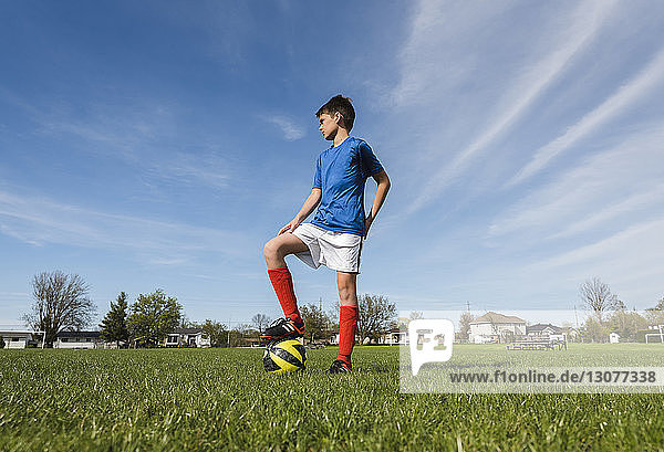 Niedrigwinkelansicht eines Jungen mit Fussball  der auf einem Rasenfeld steht
