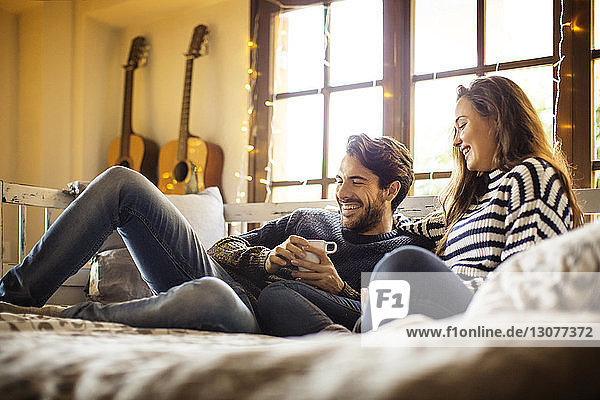 Glückliches Paar trinkt Kaffee  während es sich zu Hause auf einem Fensterplatz in einer Nische ausruht