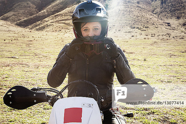 Portrait of female biker sitting on motorcycle putting on goggles