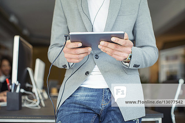Midsection of businessman using tablet computer while standing by table in office