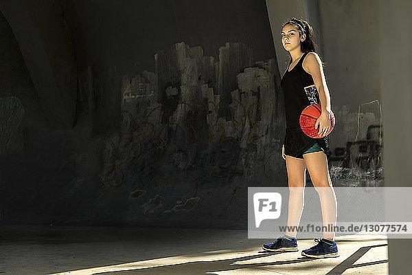Porträt eines selbstbewussten Sportlers  der Basketball hält  während er an der Wand steht