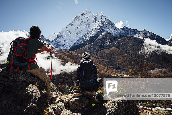 Friends with backpacks sitting on mountain against blue sky at Sagarmatha National Park