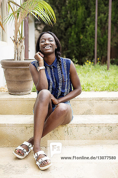 Porträt einer glücklichen Frau  die auf Stufen im Hof sitzt