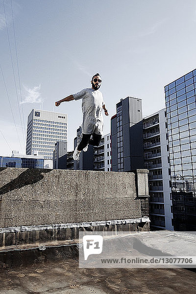 Niedrigwinkelansicht eines Mannes  der auf einer Gebäudeterrasse gegen den Himmel springt