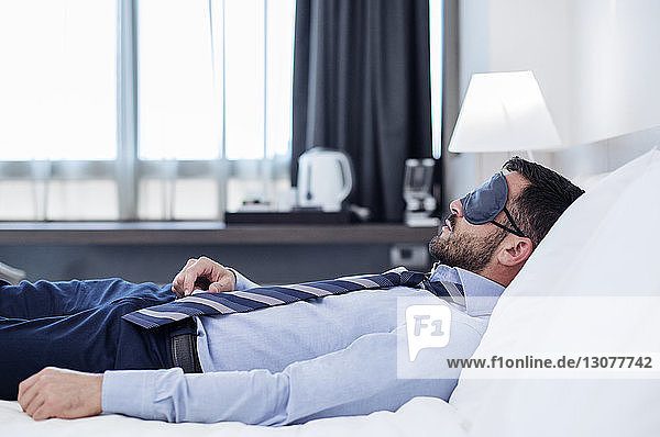 Seitenansicht eines Geschäftsmannes mit Augenmaske beim Schlafen im Hotelzimmer