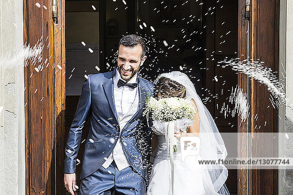 Confetti throwing on happy newlywed couple standing at church entrance
