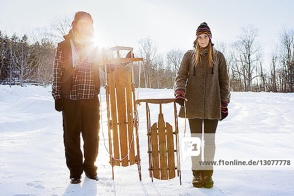 Porträt eines Ehepaares mit Schlitten auf schneebedecktem Feld stehend