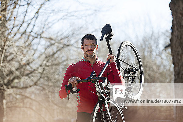 Portrait of athlete carrying bicycle in forest