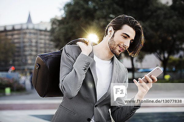Businessman carrying bag while using mobile phone