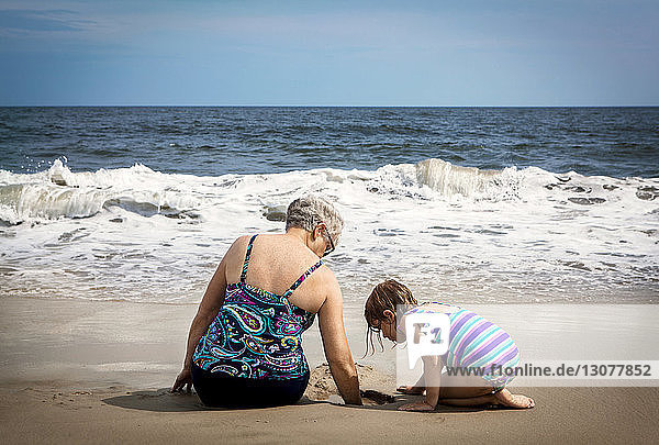 Mädchen schaut nach unten  während die Großmutter am Strand im Sand buddelt