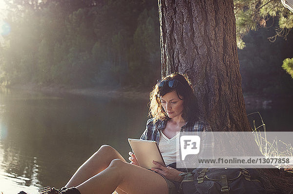 Frau benutzt Tablet-Computer  während sie am Seeufer sitzt