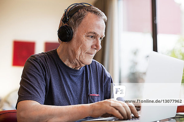 Älterer Mann hört Musik  während er zu Hause einen Laptop benutzt