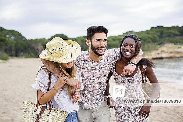 Cheerful man walking with arms around female friends on beach