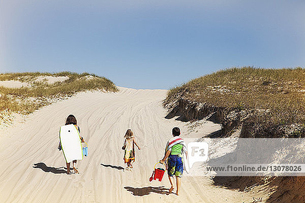 Rückansicht von Geschwistern mit Strandspielzeug  die auf Sand gegen den Himmel laufen