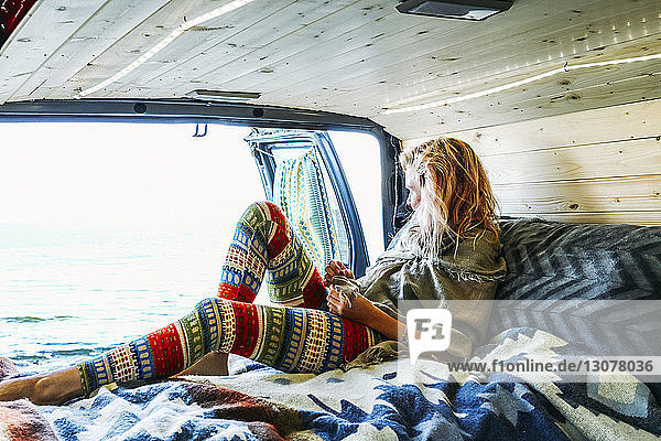 Frau schaut aufs Meer  während sie sich auf einer Matratze im Wohnwagen anlehnt