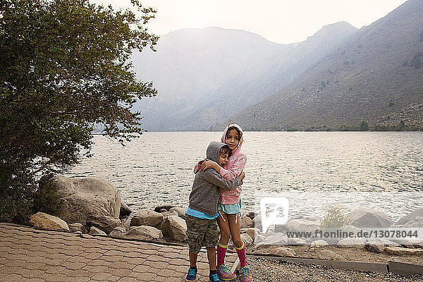 Siblings embracing and standing on field against Convict Lake and mountains