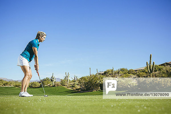 Seitenansicht einer Golf spielenden Frau auf dem Feld vor blauem Himmel