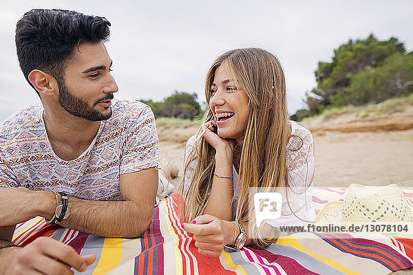 Fröhliches Paar unterhält sich im Liegen auf einer Decke am Strand