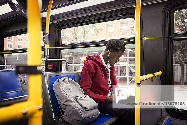 Student listening music and reading book while sitting in bus