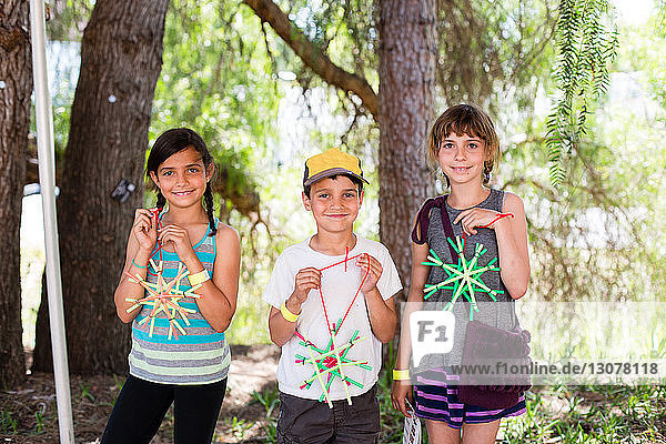Portrait of siblings holding star shaped art work while standing against trees