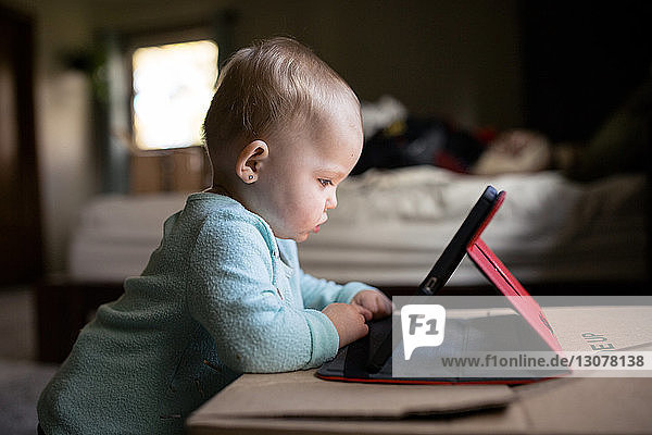 Kleines Mädchen benutzt Tablet-Computer  während es zu Hause an der Kiste steht