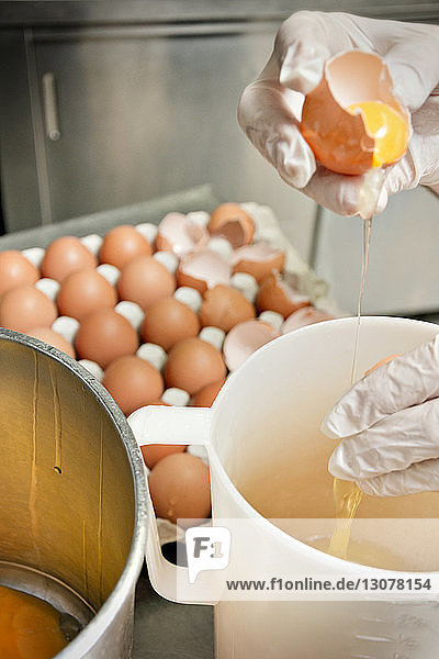 Ausgeschnittenes Bild eines Küchenchefs  der Eier in einem Glas an der Küchentheke zerbricht
