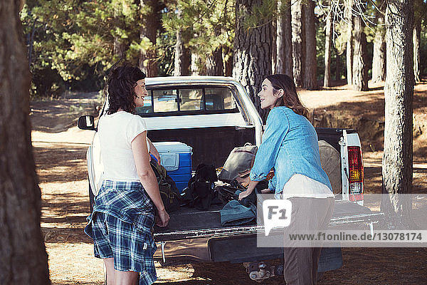 Female friends talking while standing by pick-up truck in forest