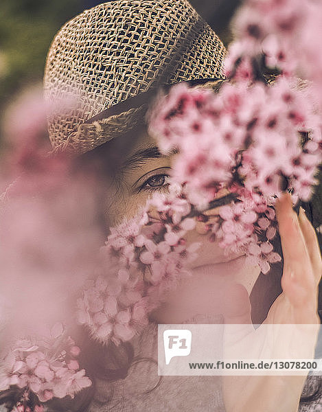 Nahaufnahme einer jungen Frau mit Kirschblüten mit Hut im Park