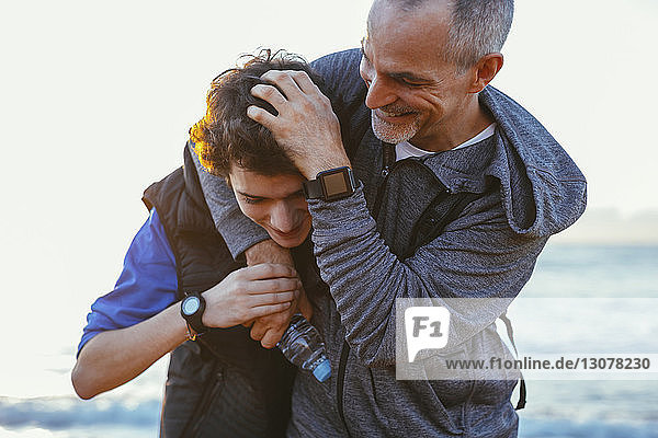 Playful father and son playing while exercising at beach against sky
