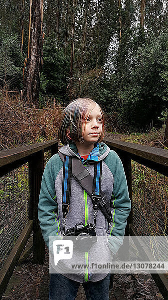 Boy with camera standing by fence in forest