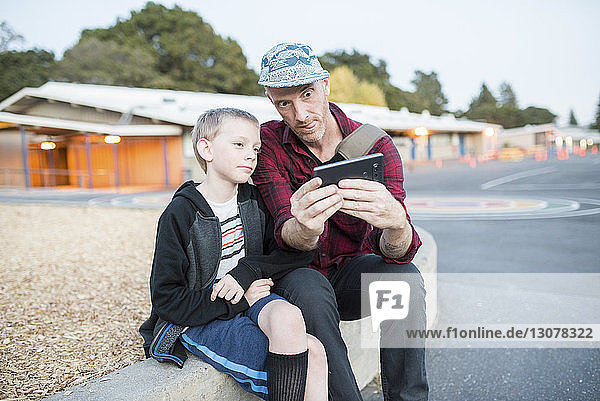 Father and son talking selfie through mobile phone while sitting on street