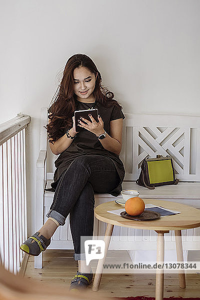 Happy woman using tablet computer while sitting on bench