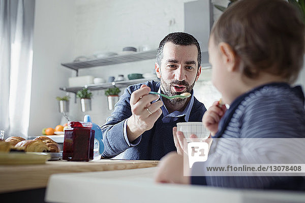 Father feeding breakfast to son sitting in high chair at home