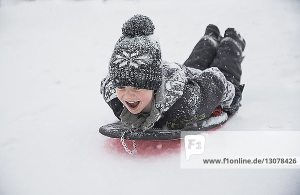 Fröhlicher Junge schlittert bei Schneefall auf Schnee