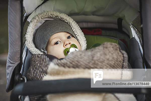 Porträt eines süßen Kleinkindes mit Schnuller im Mund  das im Herbst auf einem Kinderwagen im Park liegt