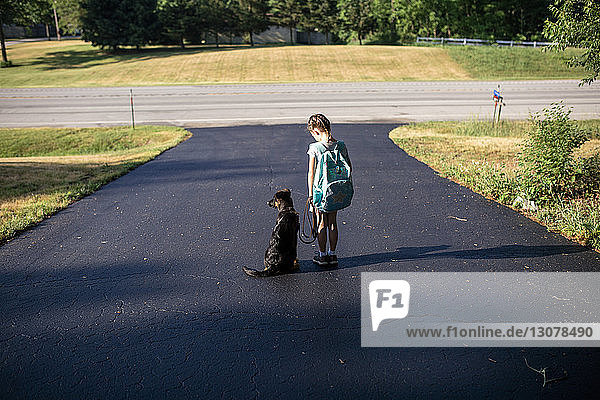 Rear view of girl carrying backpack while standing with dog on road