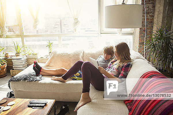 Children looking at tablet computer while sitting on sofa in living room