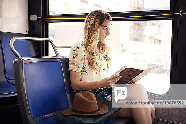 Woman reading book while traveling in bus