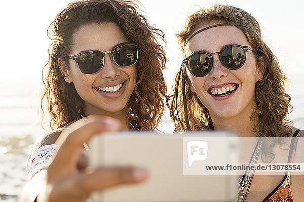 Happy female friends taking selfie at beach