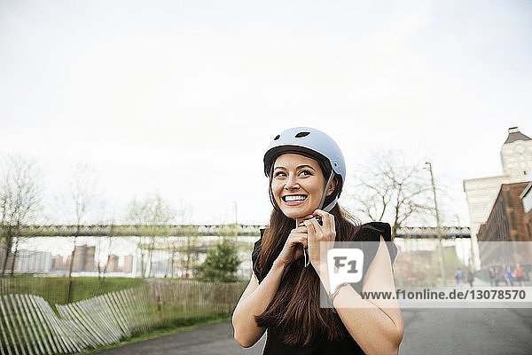 Happy woman wearing helmet while standing on road against clear sky